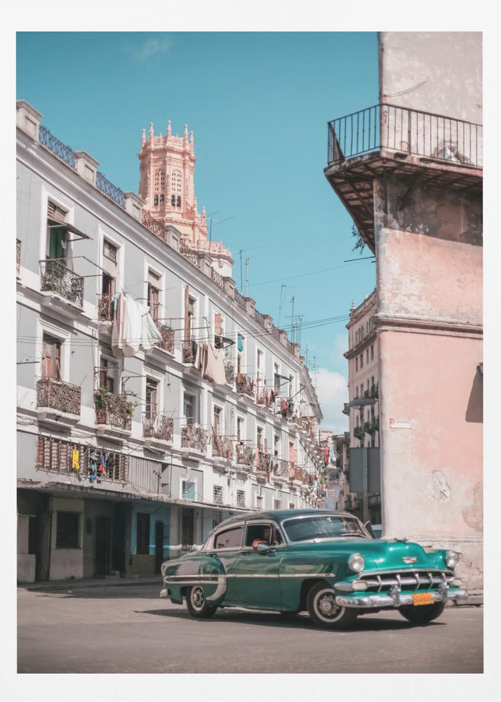 A vintage teal-green classic car sits on a sunny street in a historic city, possibly Havana, Cuba. Weathered apartment buildings with intricate balconies and hanging laundry line the street, with a peach-colored church tower visible in the background against a clear turquoise sky. Poster