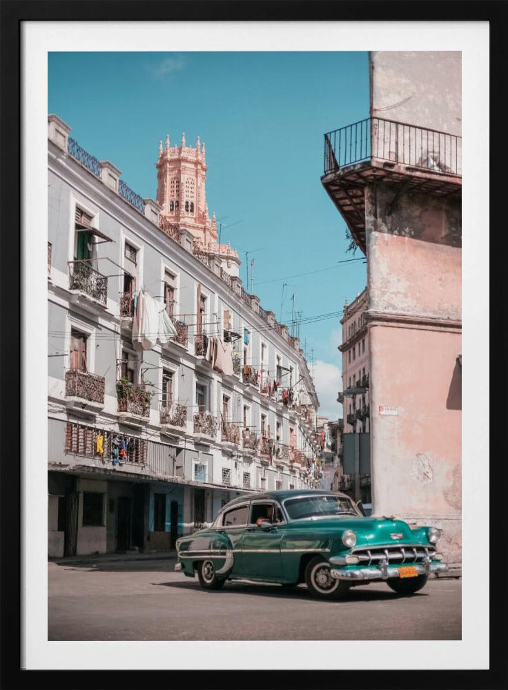 A vintage teal-green classic car sits on a sunny street in a historic city, possibly Havana, Cuba. Weathered apartment buildings with intricate balconies and hanging laundry line the street, with a peach-colored church tower visible in the background against a clear turquoise sky. Poster