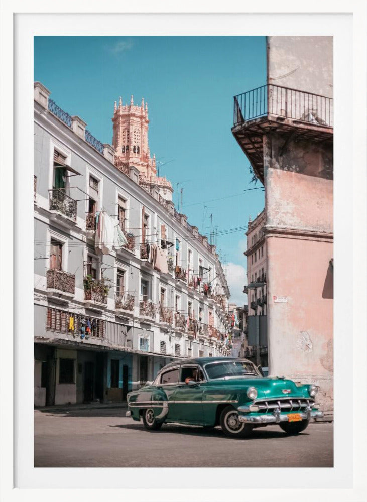 A vintage teal-green classic car sits on a sunny street in a historic city, possibly Havana, Cuba. Weathered apartment buildings with intricate balconies and hanging laundry line the street, with a peach-colored church tower visible in the background against a clear turquoise sky. Poster