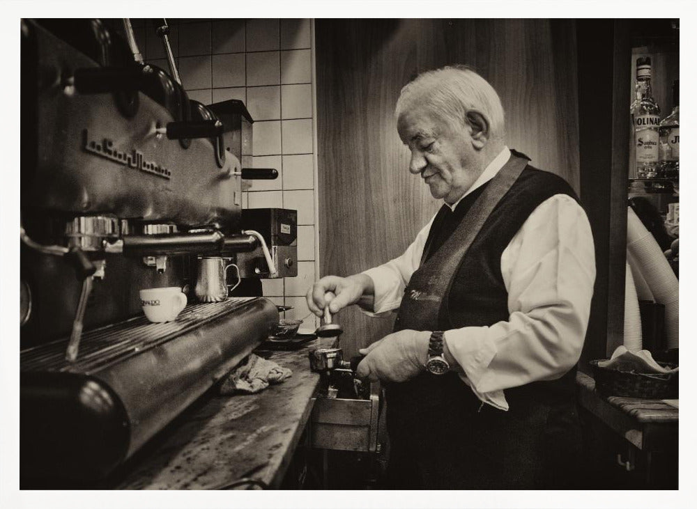 A sepia-toned, framed photograph of an elderly barista with white hair, wearing a vest, as he skillfully prepares an espresso. He is focused on his task, tamping the coffee grounds with a gentle smile, standing next to a large, vintage-style espresso machine in a cozy cafe setting. Print