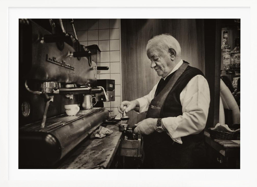 A sepia-toned, framed photograph of an elderly barista with white hair, wearing a vest, as he skillfully prepares an espresso. He is focused on his task, tamping the coffee grounds with a gentle smile, standing next to a large, vintage-style espresso machine in a cozy cafe setting. Print
