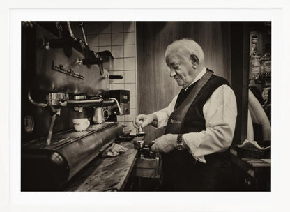 A sepia-toned, framed photograph of an elderly barista with white hair, wearing a vest, as he skillfully prepares an espresso. He is focused on his task, tamping the coffee grounds with a gentle smile, standing next to a large, vintage-style espresso machine in a cozy cafe setting. Print