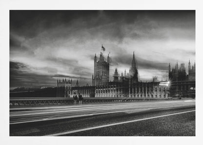 A framed, black and white long-exposure photograph of the Houses of Parliament and Big Ben in London. The view is from a bridge, with streaks of white light from traffic blurring across the road in the foreground under a dramatic, cloudy sky. Wall Art