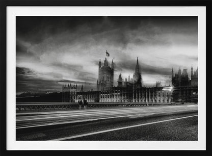 A framed, black and white long-exposure photograph of the Houses of Parliament and Big Ben in London. The view is from a bridge, with streaks of white light from traffic blurring across the road in the foreground under a dramatic, cloudy sky. Wall Art