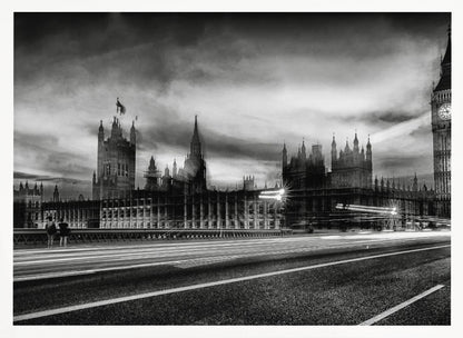 A framed, black and white long-exposure photograph of the Houses of Parliament and Big Ben in London. The view is from a bridge, with streaks of white light from traffic blurring across the road in the foreground under a dramatic, cloudy sky. Wall Art