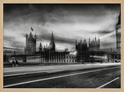 A framed, black and white long-exposure photograph of the Houses of Parliament and Big Ben in London. The view is from a bridge, with streaks of white light from traffic blurring across the road in the foreground under a dramatic, cloudy sky. Wall Art