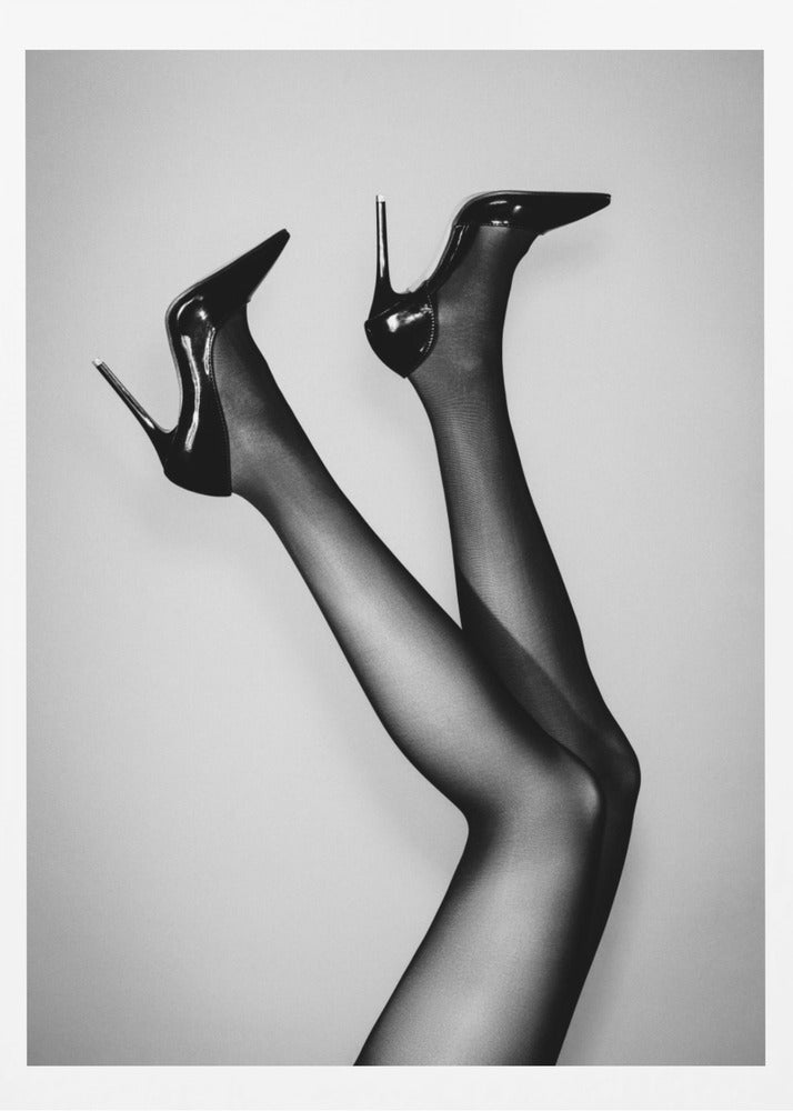 A black and white photograph of a woman's legs in the air, wearing sheer black stockings and shiny black stiletto high heels against a plain grey background. Poster