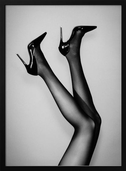 A black and white photograph of a woman's legs in the air, wearing sheer black stockings and shiny black stiletto high heels against a plain grey background. Poster