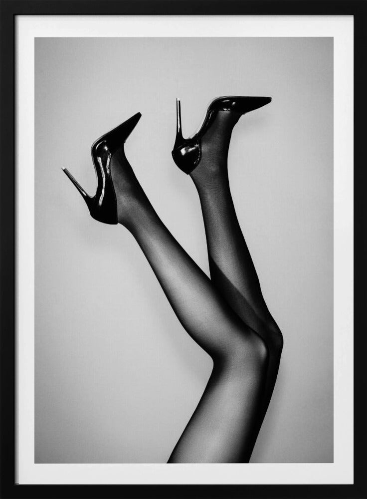 A black and white photograph of a woman's legs in the air, wearing sheer black stockings and shiny black stiletto high heels against a plain grey background. Poster