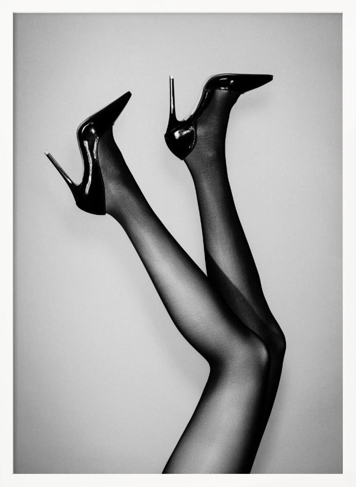 A black and white photograph of a woman's legs in the air, wearing sheer black stockings and shiny black stiletto high heels against a plain grey background. Poster