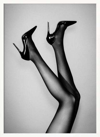 A black and white photograph of a woman's legs in the air, wearing sheer black stockings and shiny black stiletto high heels against a plain grey background. Poster