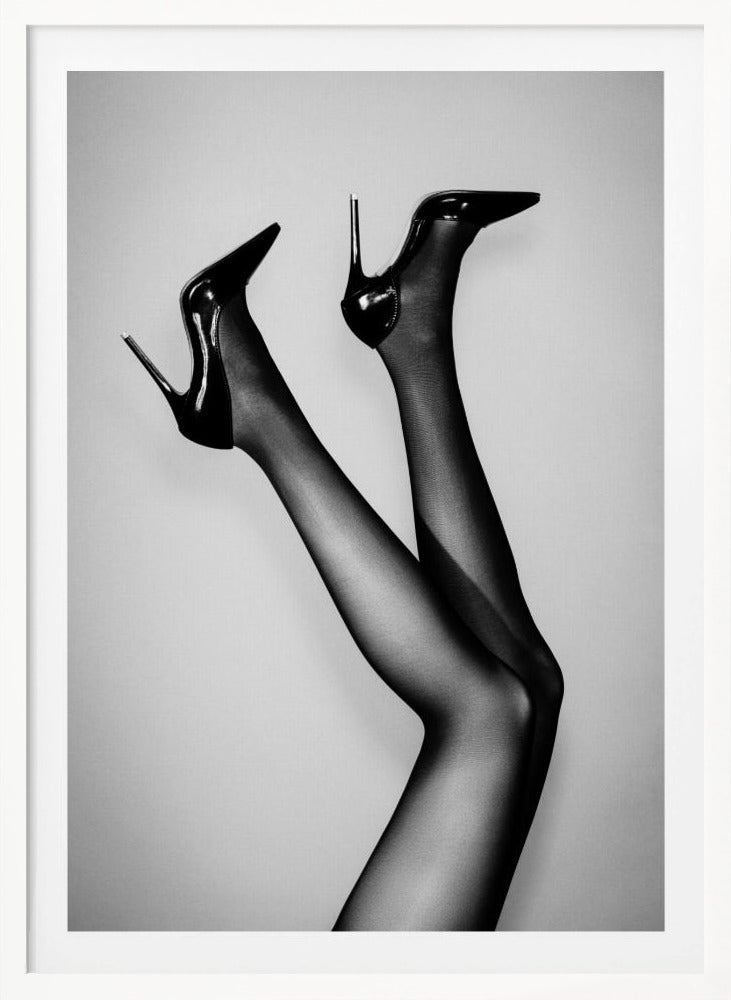 A black and white photograph of a woman's legs in the air, wearing sheer black stockings and shiny black stiletto high heels against a plain grey background. Poster