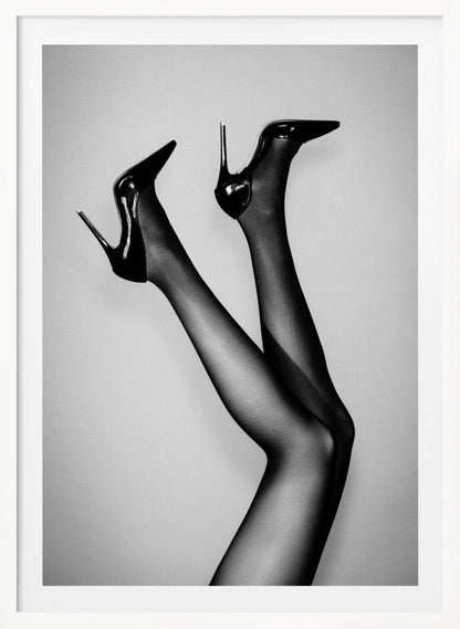 A black and white photograph of a woman's legs in the air, wearing sheer black stockings and shiny black stiletto high heels against a plain grey background. Poster