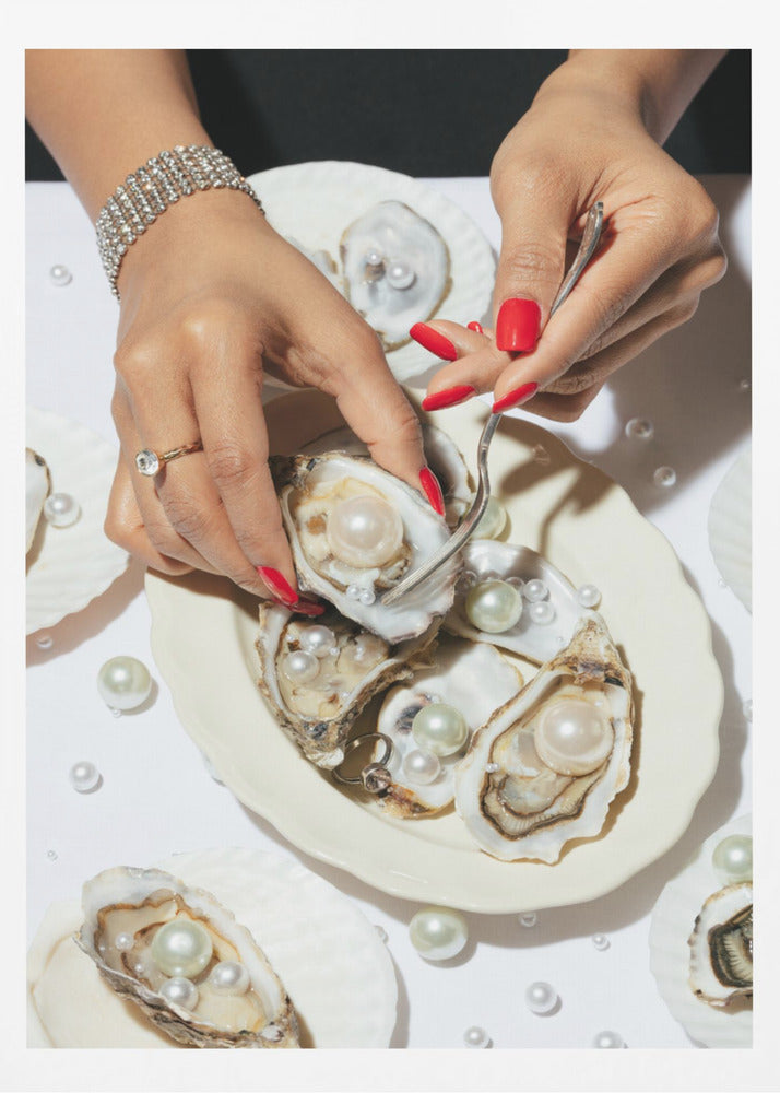 A close-up overhead shot of a woman's hands with vibrant red nails and elegant jewelry, using a fork to lift a large pearl from an oyster shell on a white plate. The plate and the surrounding white surface are adorned with numerous oysters filled with pearls of varying sizes, creating a luxurious and surreal scene. Print