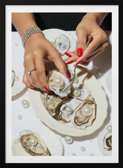 A close-up overhead shot of a woman's hands with vibrant red nails and elegant jewelry, using a fork to lift a large pearl from an oyster shell on a white plate. The plate and the surrounding white surface are adorned with numerous oysters filled with pearls of varying sizes, creating a luxurious and surreal scene. Print