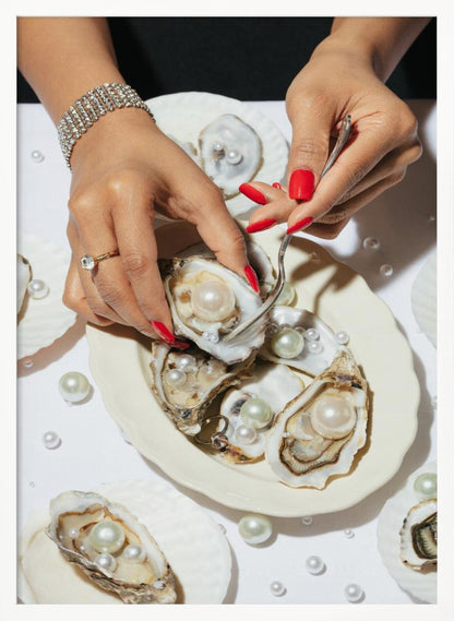 A close-up overhead shot of a woman's hands with vibrant red nails and elegant jewelry, using a fork to lift a large pearl from an oyster shell on a white plate. The plate and the surrounding white surface are adorned with numerous oysters filled with pearls of varying sizes, creating a luxurious and surreal scene. Print