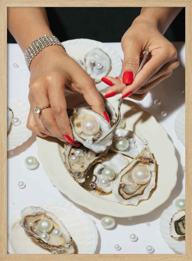 A close-up overhead shot of a woman's hands with vibrant red nails and elegant jewelry, using a fork to lift a large pearl from an oyster shell on a white plate. The plate and the surrounding white surface are adorned with numerous oysters filled with pearls of varying sizes, creating a luxurious and surreal scene. Print