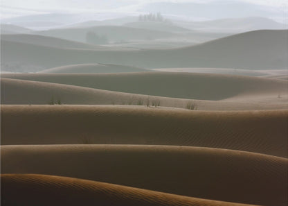 A framed photograph of a serene desert landscape, with layers of rolling sand dunes creating a sense of depth. Dark brown dunes in the foreground give way to lighter, hazy dunes and hills in the misty background. Print
