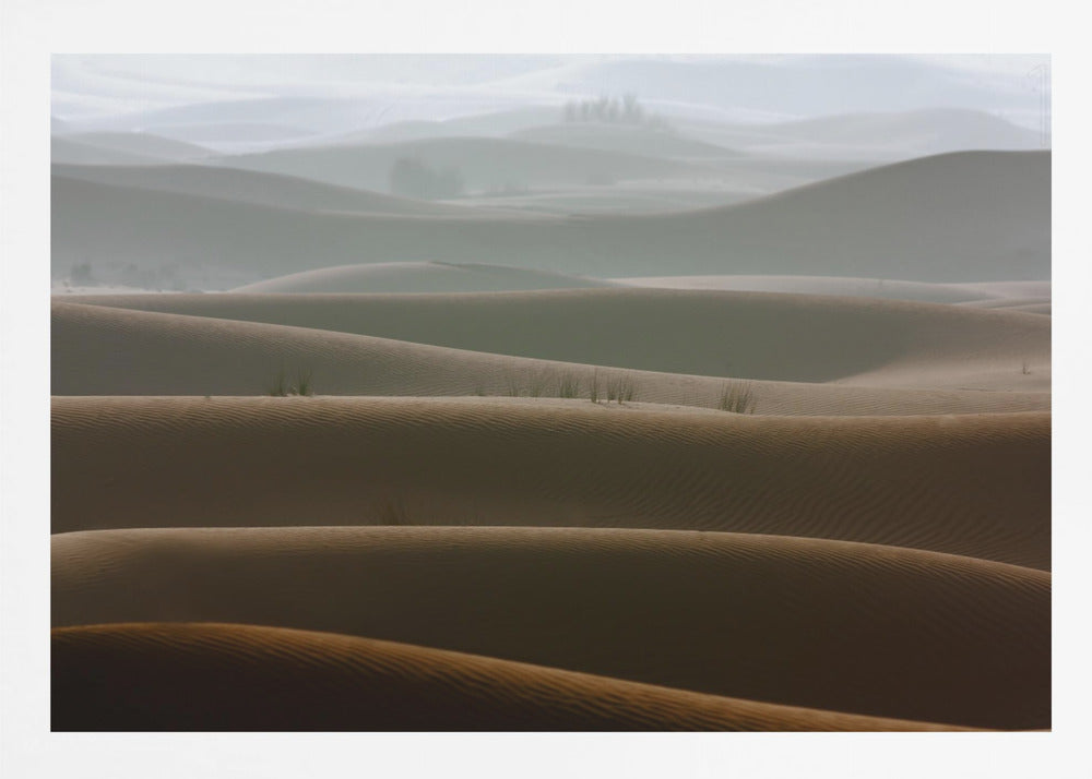 A framed photograph of a serene desert landscape, with layers of rolling sand dunes creating a sense of depth. Dark brown dunes in the foreground give way to lighter, hazy dunes and hills in the misty background. Print