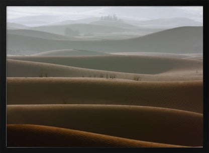 A framed photograph of a serene desert landscape, with layers of rolling sand dunes creating a sense of depth. Dark brown dunes in the foreground give way to lighter, hazy dunes and hills in the misty background. Print
