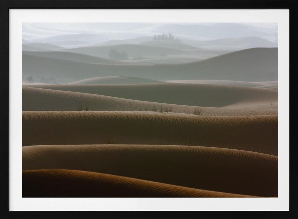 A framed photograph of a serene desert landscape, with layers of rolling sand dunes creating a sense of depth. Dark brown dunes in the foreground give way to lighter, hazy dunes and hills in the misty background. Print