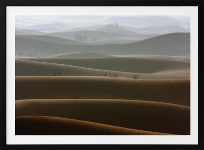 A framed photograph of a serene desert landscape, with layers of rolling sand dunes creating a sense of depth. Dark brown dunes in the foreground give way to lighter, hazy dunes and hills in the misty background. Print