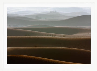 A framed photograph of a serene desert landscape, with layers of rolling sand dunes creating a sense of depth. Dark brown dunes in the foreground give way to lighter, hazy dunes and hills in the misty background. Print