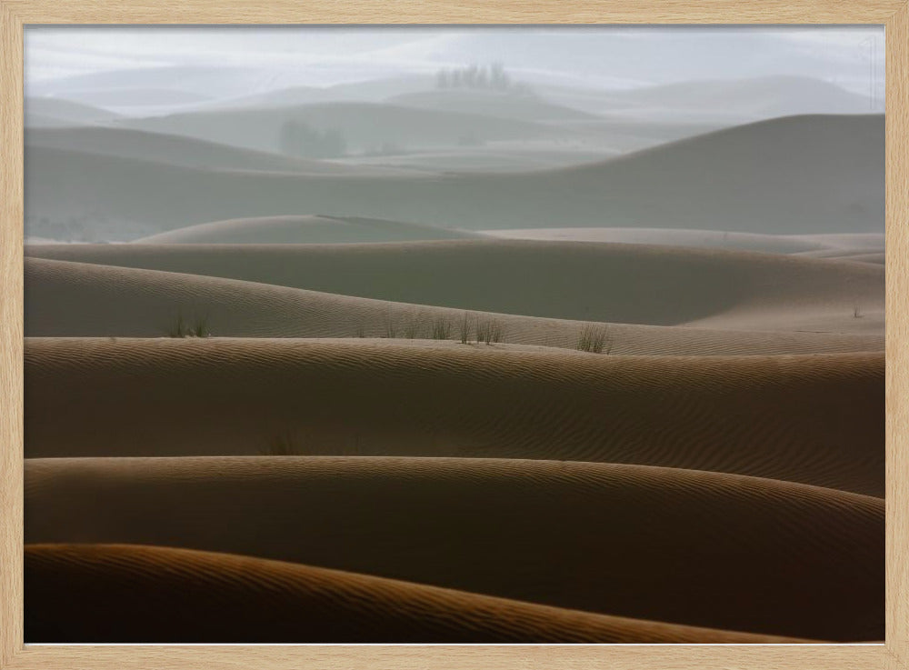A framed photograph of a serene desert landscape, with layers of rolling sand dunes creating a sense of depth. Dark brown dunes in the foreground give way to lighter, hazy dunes and hills in the misty background. Print