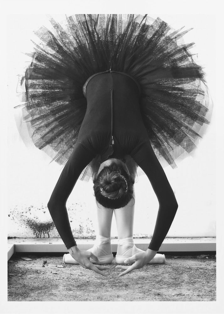 A striking black and white photograph of a ballerina in a deep forward bend. Her body is clad in a black leotard and white tights, with a voluminous black tutu fanning out vertically behind her. Her hair is tied in a bun, and her hands gracefully reach towards her feet, which are in white pointe shoes. Artwork