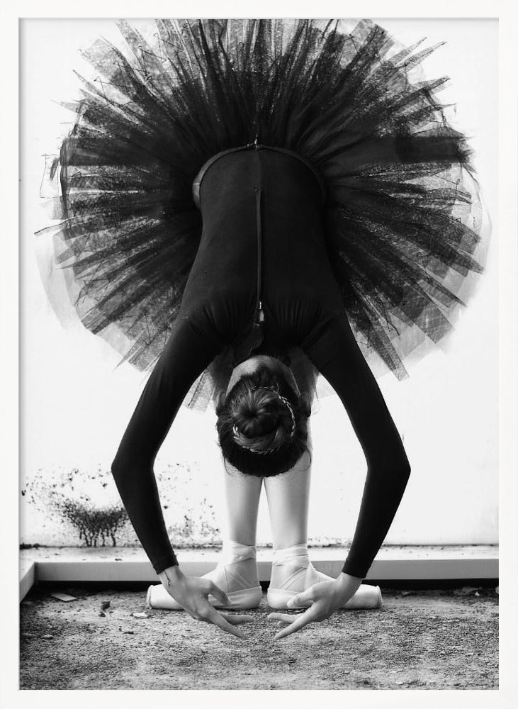 A striking black and white photograph of a ballerina in a deep forward bend. Her body is clad in a black leotard and white tights, with a voluminous black tutu fanning out vertically behind her. Her hair is tied in a bun, and her hands gracefully reach towards her feet, which are in white pointe shoes. Artwork