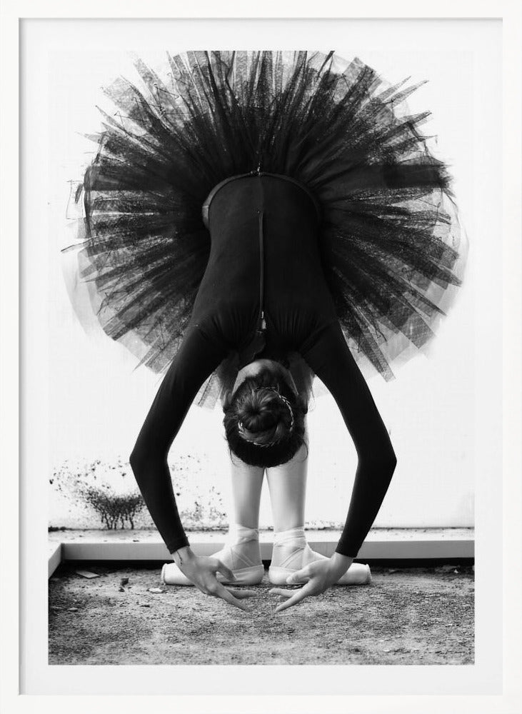 A striking black and white photograph of a ballerina in a deep forward bend. Her body is clad in a black leotard and white tights, with a voluminous black tutu fanning out vertically behind her. Her hair is tied in a bun, and her hands gracefully reach towards her feet, which are in white pointe shoes. Artwork