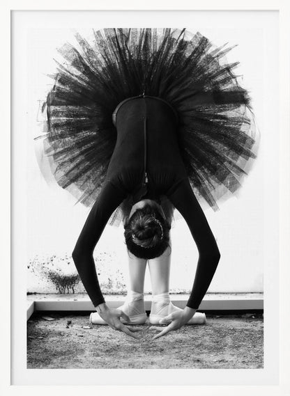 A striking black and white photograph of a ballerina in a deep forward bend. Her body is clad in a black leotard and white tights, with a voluminous black tutu fanning out vertically behind her. Her hair is tied in a bun, and her hands gracefully reach towards her feet, which are in white pointe shoes. Artwork