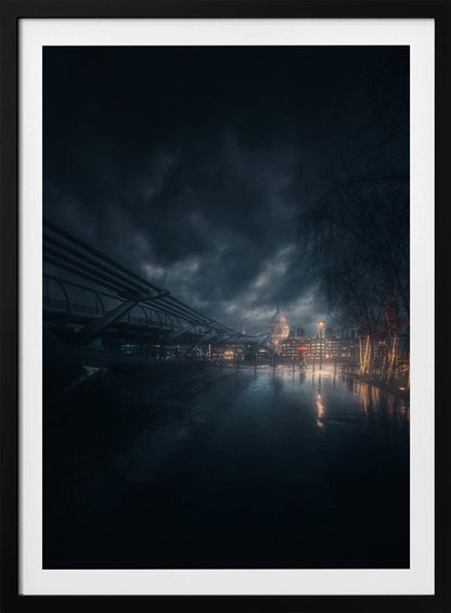 A moody, atmospheric night photograph of London, featuring the Millennium Bridge stretching across a wet surface towards the illuminated St. Paul's Cathedral under a dark, stormy sky. City lights reflect on the wet ground, and trees with warm lights line the right side of the frame. Artwork