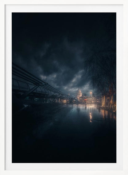A moody, atmospheric night photograph of London, featuring the Millennium Bridge stretching across a wet surface towards the illuminated St. Paul's Cathedral under a dark, stormy sky. City lights reflect on the wet ground, and trees with warm lights line the right side of the frame. Artwork