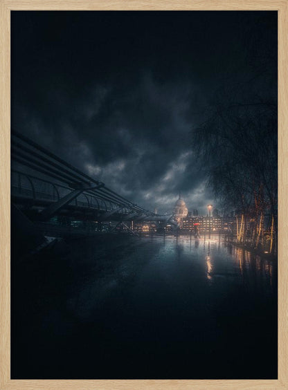 A moody, atmospheric night photograph of London, featuring the Millennium Bridge stretching across a wet surface towards the illuminated St. Paul's Cathedral under a dark, stormy sky. City lights reflect on the wet ground, and trees with warm lights line the right side of the frame. Artwork