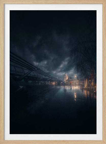 A moody, atmospheric night photograph of London, featuring the Millennium Bridge stretching across a wet surface towards the illuminated St. Paul's Cathedral under a dark, stormy sky. City lights reflect on the wet ground, and trees with warm lights line the right side of the frame. Artwork