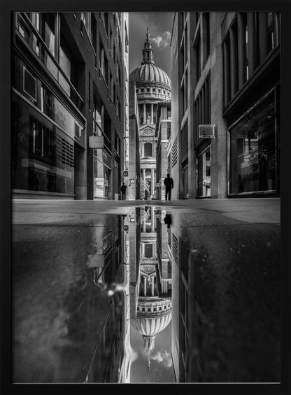 A dramatic black and white photograph taken from a low angle on a narrow city street, perfectly framing St. Paul's Cathedral in the distance. The foreground is dominated by a large puddle, which creates a stunning, clear reflection of the entire scene, including the cathedral, buildings, and sky. Print