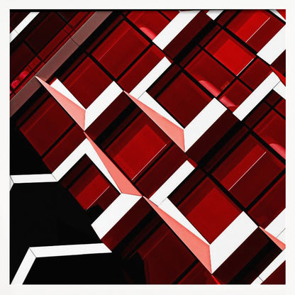 A close-up, angular photograph of a modern building's facade, framed in light wood. The composition is a dynamic geometric pattern of glossy red square panels, stark white lines, and deep black shadows, creating a sense of depth and abstract complexity. Wall Art