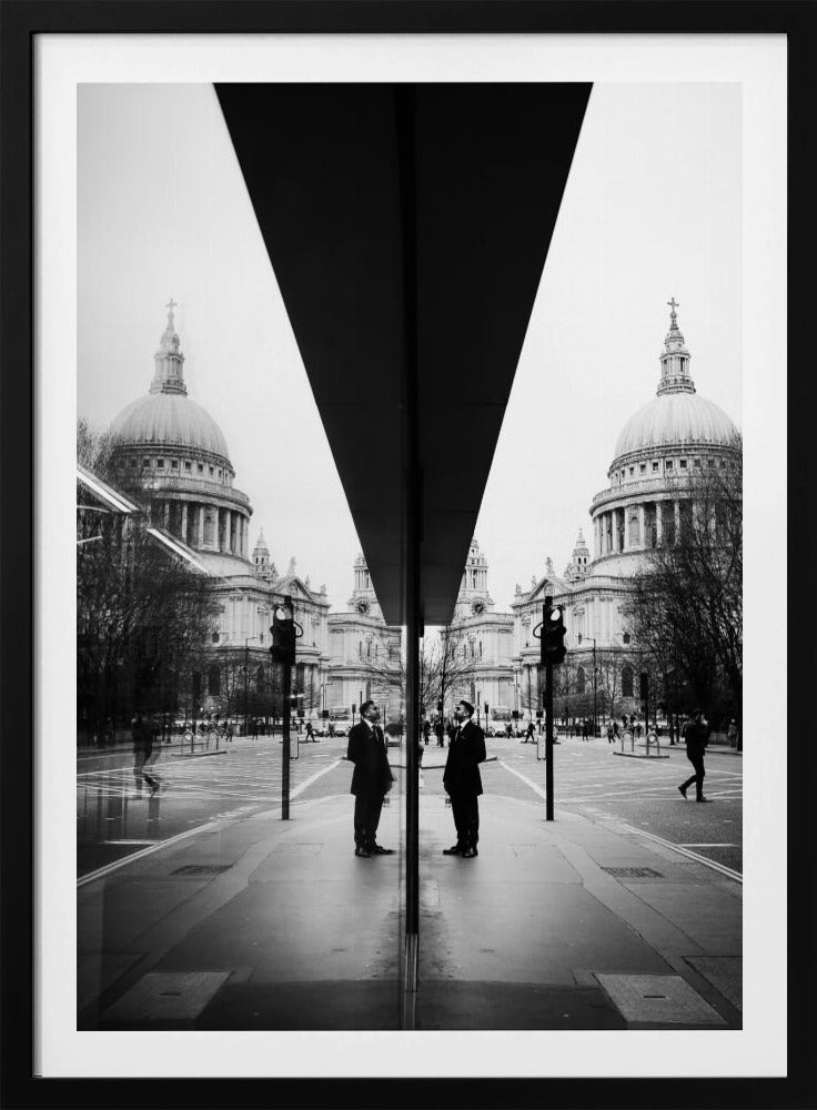 A surreal black and white photograph capturing a symmetrical reflection of a city scene, with St. Paul's Cathedral prominently featured on both sides. A dark, V-shaped reflection from a building divides the image vertically. In the foreground, the reflection of two men in dark suits standing on the sidewalk adds a human element to the grand architectural view. Decor