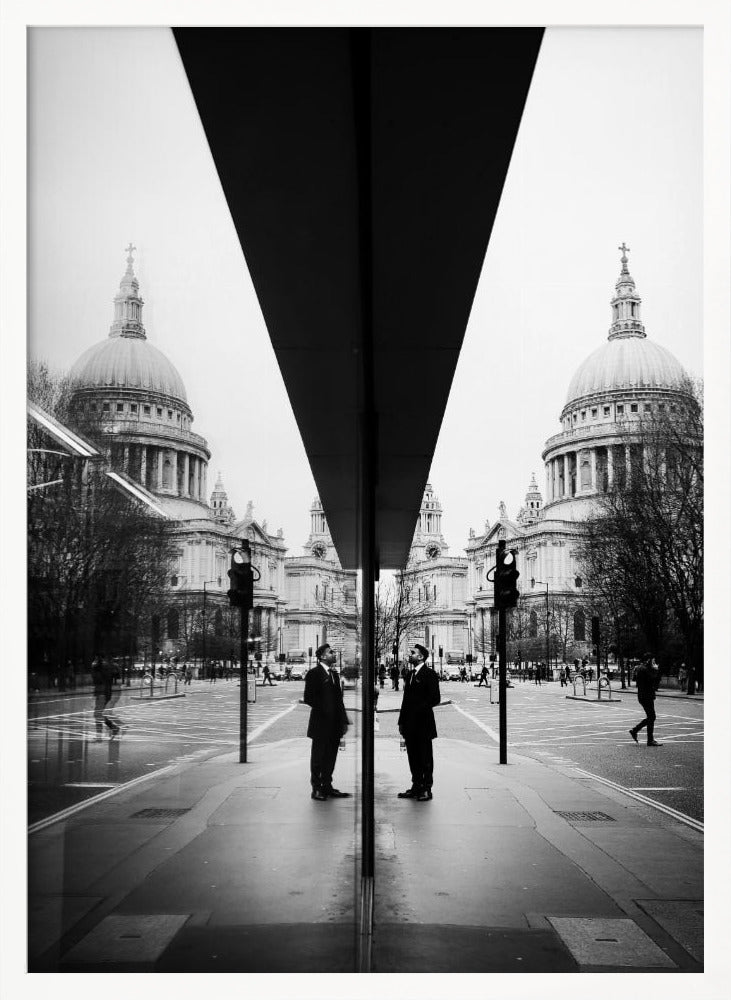 A surreal black and white photograph capturing a symmetrical reflection of a city scene, with St. Paul's Cathedral prominently featured on both sides. A dark, V-shaped reflection from a building divides the image vertically. In the foreground, the reflection of two men in dark suits standing on the sidewalk adds a human element to the grand architectural view. Decor