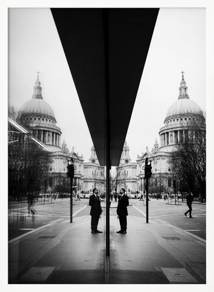 A surreal black and white photograph capturing a symmetrical reflection of a city scene, with St. Paul's Cathedral prominently featured on both sides. A dark, V-shaped reflection from a building divides the image vertically. In the foreground, the reflection of two men in dark suits standing on the sidewalk adds a human element to the grand architectural view. Decor