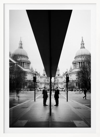 A surreal black and white photograph capturing a symmetrical reflection of a city scene, with St. Paul's Cathedral prominently featured on both sides. A dark, V-shaped reflection from a building divides the image vertically. In the foreground, the reflection of two men in dark suits standing on the sidewalk adds a human element to the grand architectural view. Decor