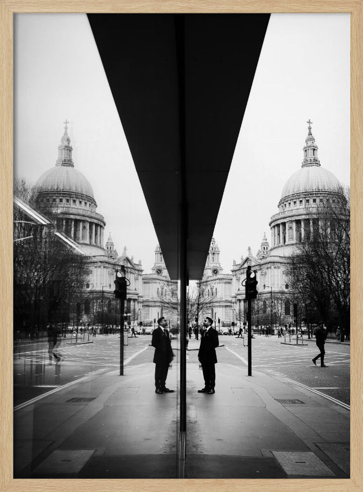 A surreal black and white photograph capturing a symmetrical reflection of a city scene, with St. Paul's Cathedral prominently featured on both sides. A dark, V-shaped reflection from a building divides the image vertically. In the foreground, the reflection of two men in dark suits standing on the sidewalk adds a human element to the grand architectural view. Decor