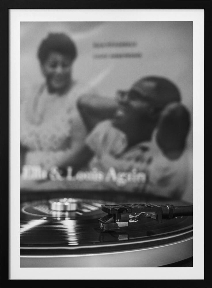 A black and white photograph focusing on a turntable's stylus resting on a spinning vinyl record. In the blurred background, the album cover for 'Ella & Louis Again' featuring Ella Fitzgerald and Louis Armstrong is visible. Poster