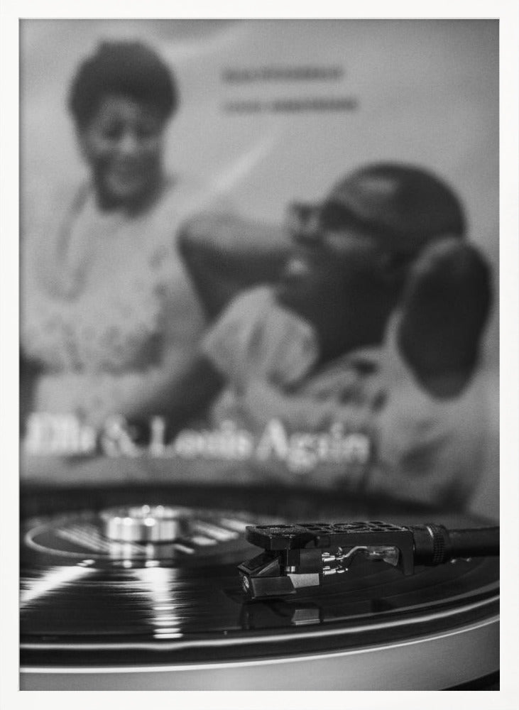 A black and white photograph focusing on a turntable's stylus resting on a spinning vinyl record. In the blurred background, the album cover for 'Ella & Louis Again' featuring Ella Fitzgerald and Louis Armstrong is visible. Poster