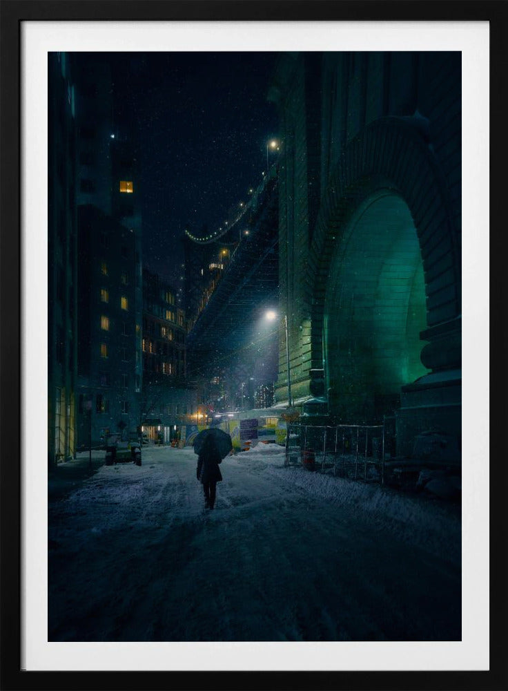 A lone person holding an umbrella walks down a snow-covered street at night, dwarfed by the massive, green-lit stone archway of the Brooklyn Bridge as snow falls around them. Print
