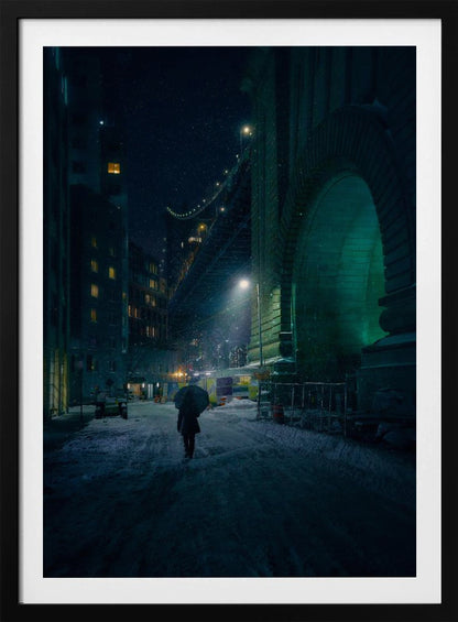 A lone person holding an umbrella walks down a snow-covered street at night, dwarfed by the massive, green-lit stone archway of the Brooklyn Bridge as snow falls around them. Print