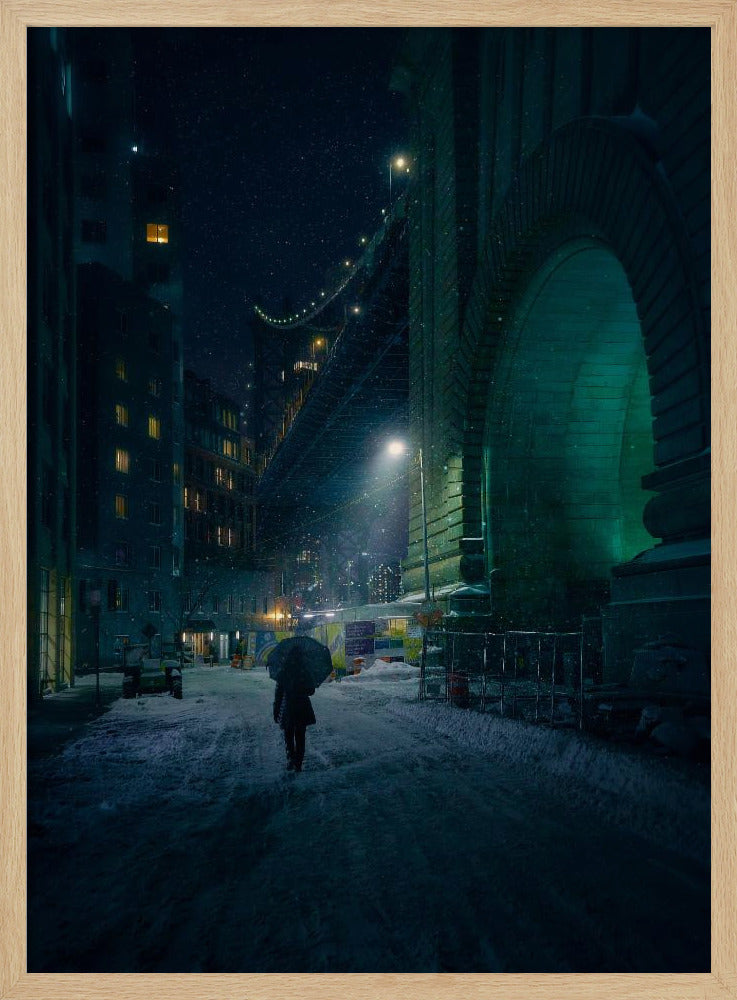A lone person holding an umbrella walks down a snow-covered street at night, dwarfed by the massive, green-lit stone archway of the Brooklyn Bridge as snow falls around them. Print