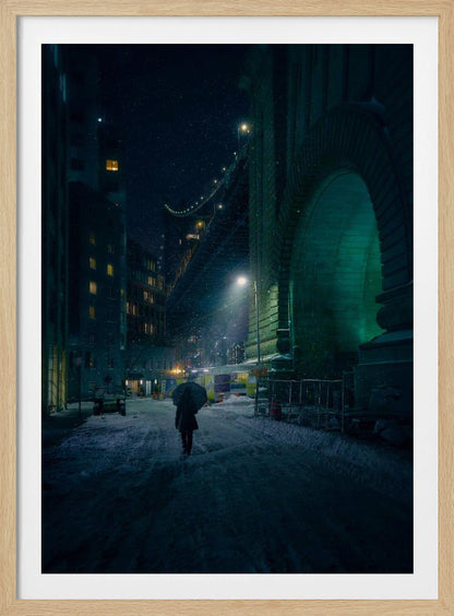A lone person holding an umbrella walks down a snow-covered street at night, dwarfed by the massive, green-lit stone archway of the Brooklyn Bridge as snow falls around them. Print
