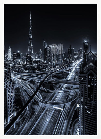 A cool-toned black and white photograph of the Dubai skyline at night. The iconic Burj Khalifa stands tall in the background, while the foreground is dominated by a massive, complex highway interchange with light trails from moving cars, creating a sense of motion and modernity. Poster